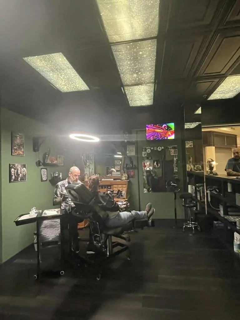 The shop floor at Legacy Tattoo Company, with an artist tattooing a client under sparkling ceiling panels